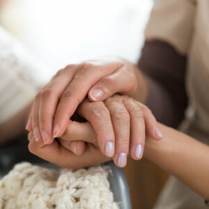 Close-up photo of a female caregiver and senior woman holding hands. Senior care concept.