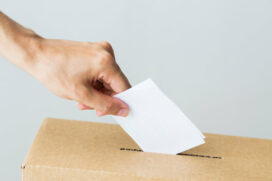 man's hand placing ballot into box voting